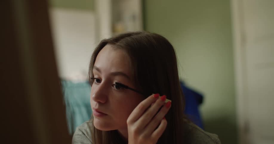 Teenage girl looks in mirror while putting on mascara