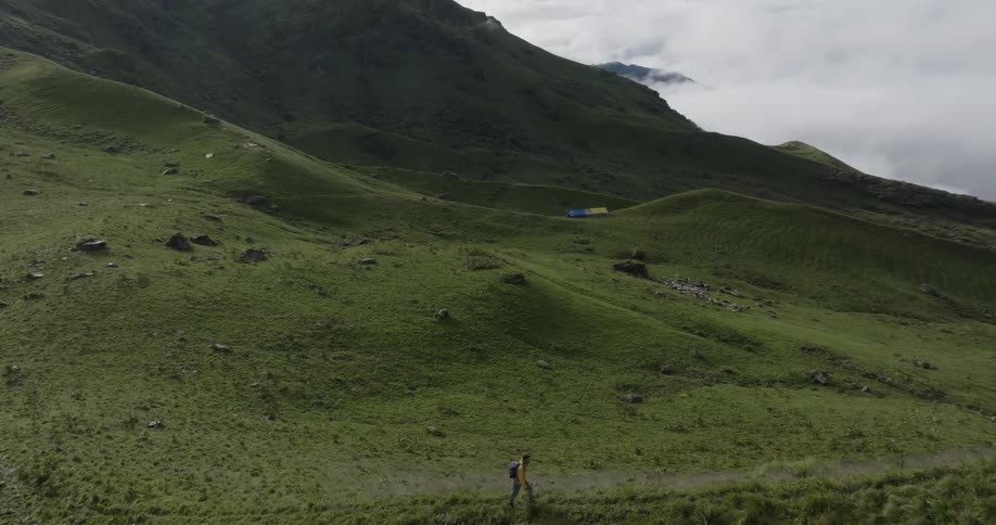 A man with a camping backpack walking over a mountain of grass and behind huge mountains of ice