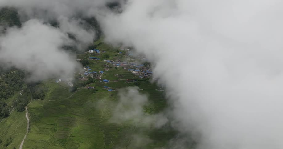 Aerial of clouds covering the land over a developing nation with grass covered hillsides
