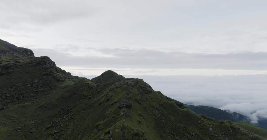 Rocks and boulders are scattered across a grass covered mountain ridge high above the clouds