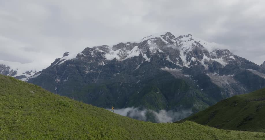 Aerial view of a man hiking on the hills next to a mountain range