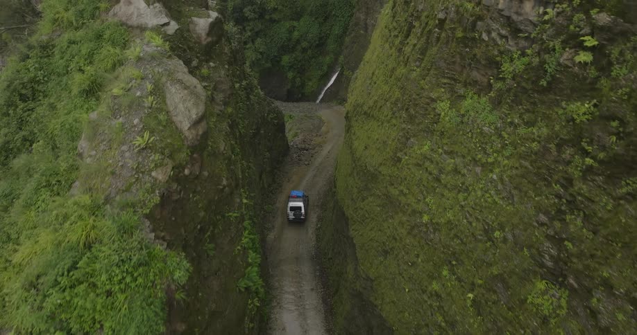 Aerial view of a white car driving through a narrow green canyon