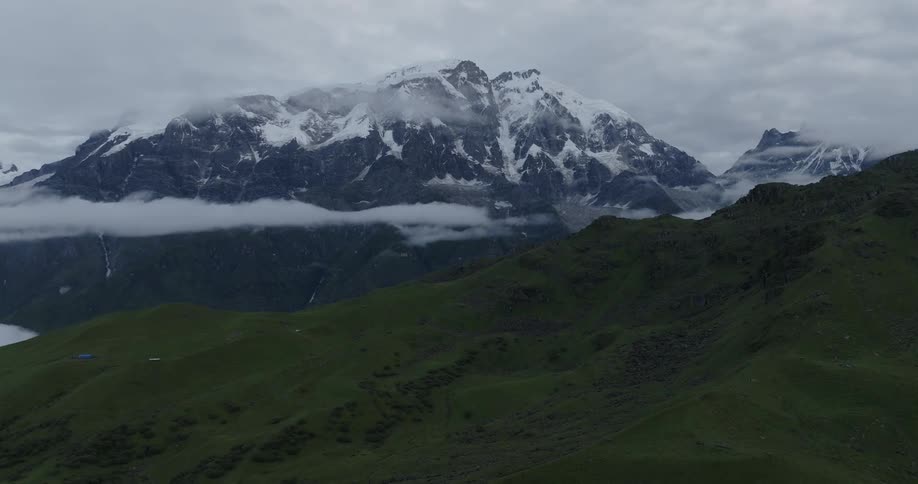 Drone view of grass covered mountain ridges and snow covered peaks in the distance with fog hovering in the valley