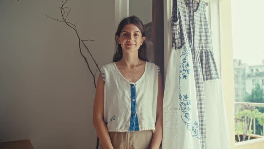 A woman standing next to a large window turns to smile into the camera