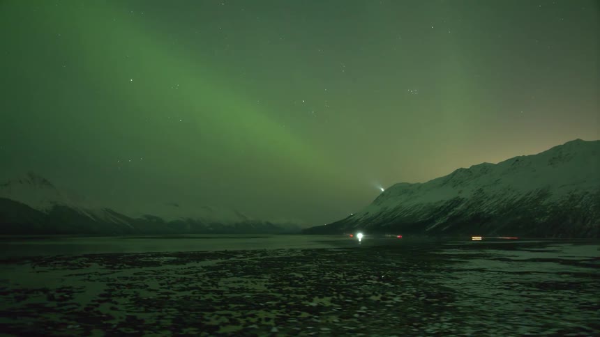 A remote region with some cars passing by with flashlights on and stars passing quickly in the sky