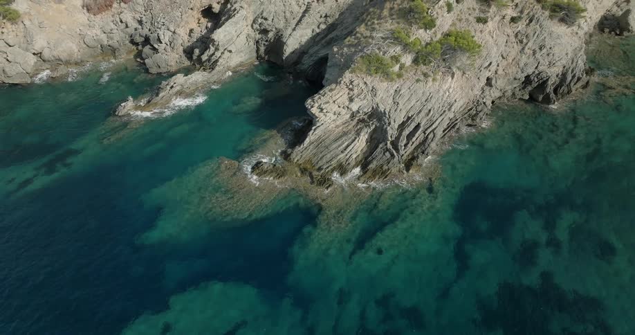 Waves crash against the base of cliffs bordering forest