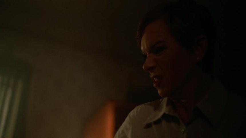 Mad woman with red short hair earrings and brown shirt sways a stick in dark room