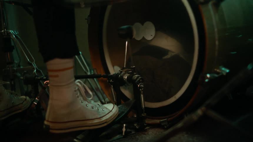 A human foot presses a pedal to hit a drum