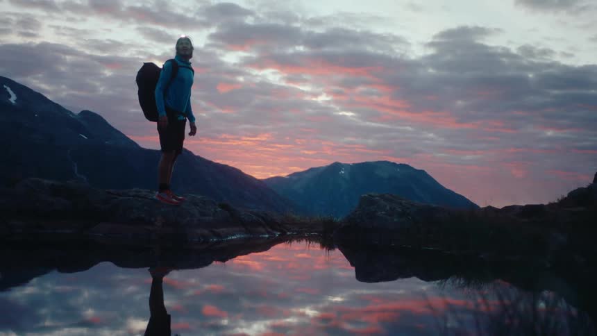 A man walks on the mountain with a lake during sunset