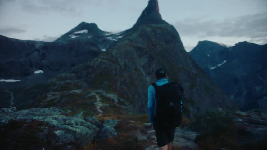 Backpacker hikes along trail across from snow dotted mountains