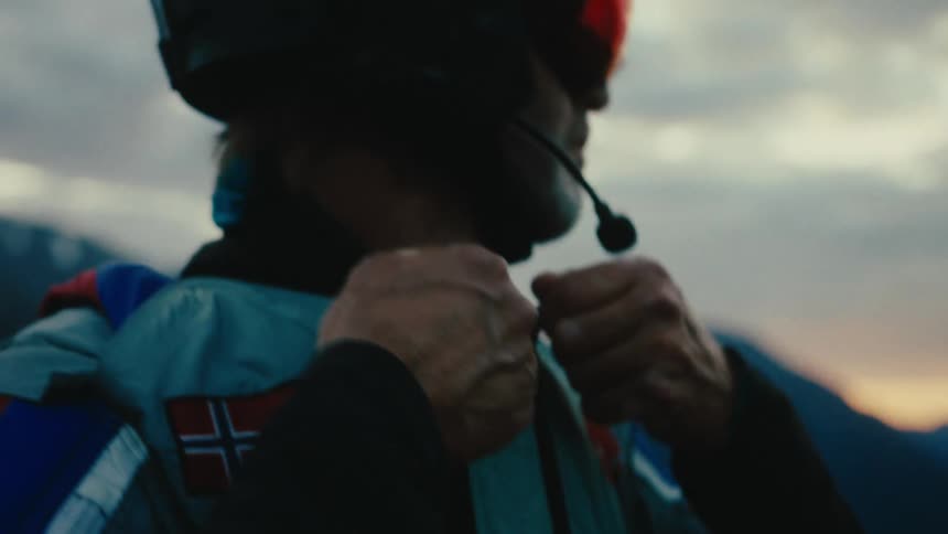 Man wearing a crash helmet suits up with a wingsuit in the mountains at sunset
