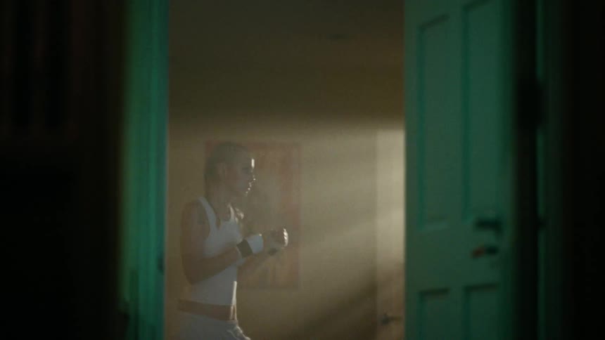 A woman is training by punching something while sunlight illuminates her