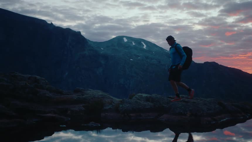 A man walks on the mountain with his reflection reflecting in the water