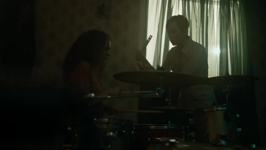 A girl and her teacher are playing the drums in a dark room