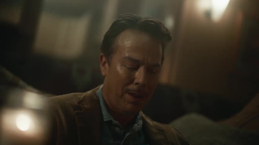 A man in suit sits in a dark place with his eyes closed