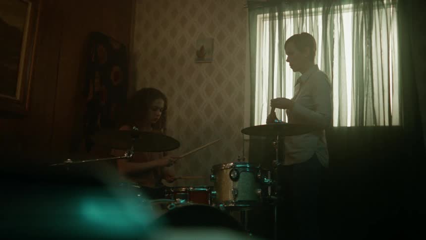 A woman playing the drums while another woman watches