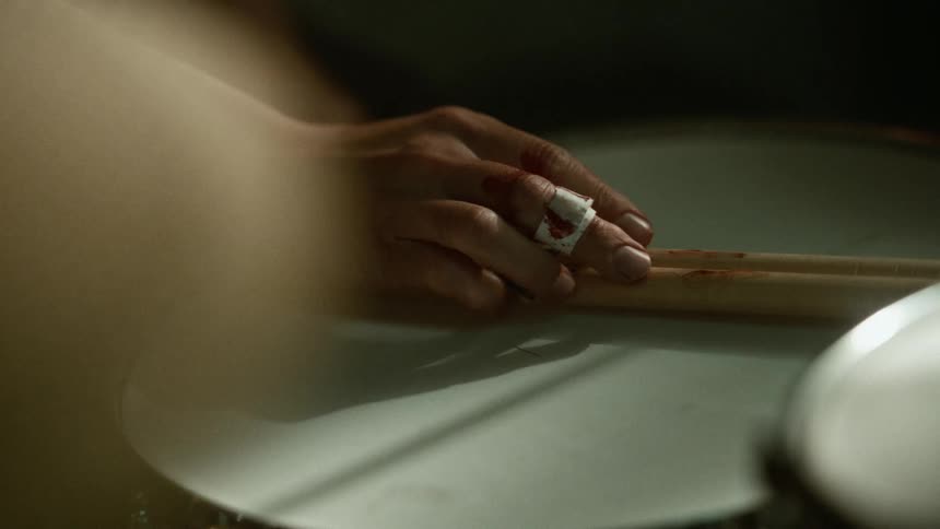 Hand of a drummer touching drumsticks resting over a drum
