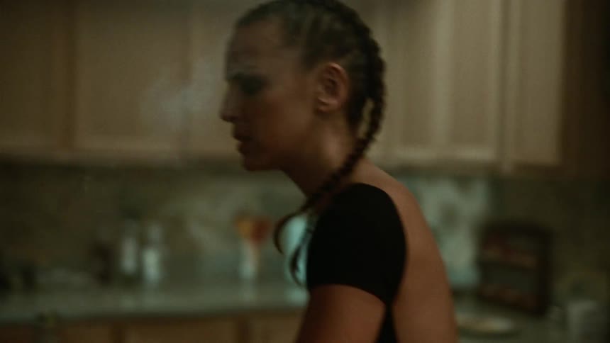 A woman walking inside the kitchen and smoking and drinking
