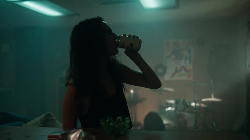 Young rocker woman drinks beer in front of a drum kit at home