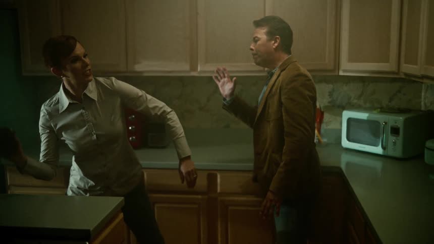 An aggressive woman pushing the man in the kitchen