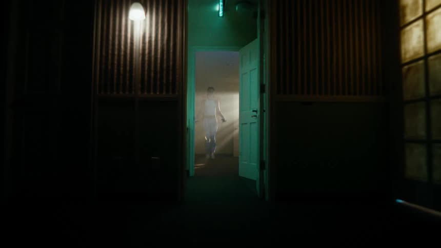 A woman inside a room is jumping rope and outside the room it is dark