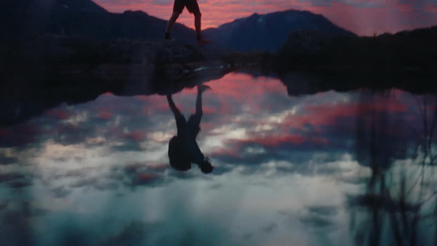 Reflection on a lake of a man hiking on the mountains at sunset