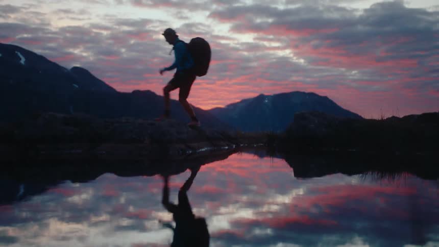 A man jumps over a mountain lake at sunset