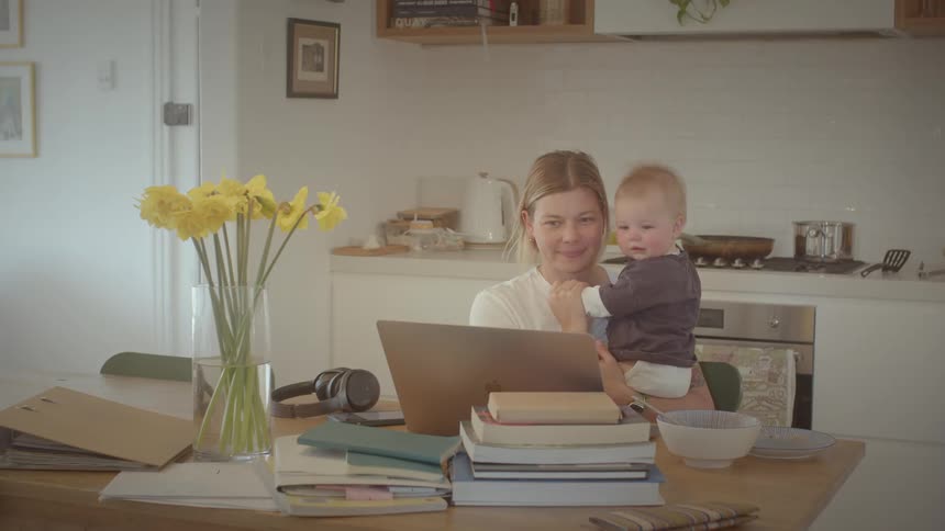 A mother sitting and holding her baby in her lap both smiling and looking at the laptop