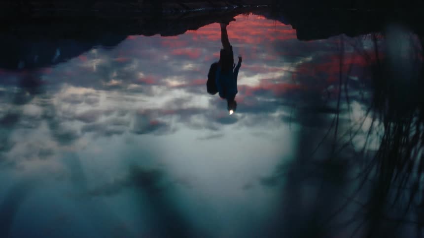The reflection of a man wearing camp clothes in a puddle of water