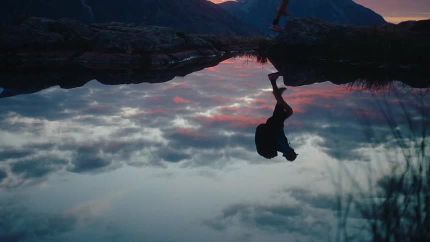 A man walking through mountainous nature with his reflection in a lake on a sunrise day with a red sky