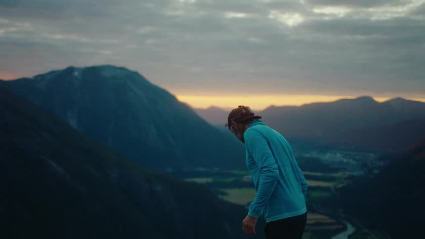 A man is walking above a mountain river valley as he waves to someone below