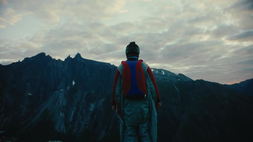 Man wearing wingsuit spreads his arms while standing on cliff
