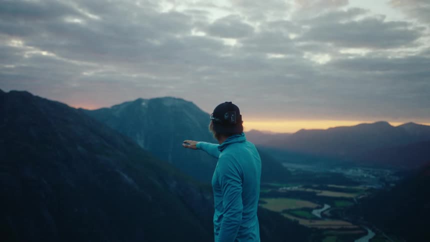 A man on top of a cliff looking at the landscape at sunset