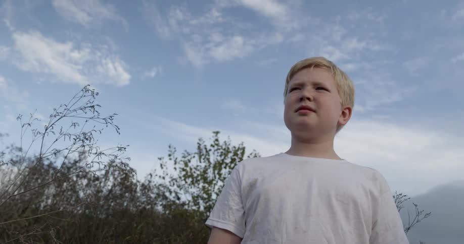 A boy is standing in front of bushes looking around