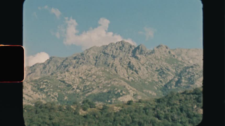 Super 8 footage of a landscape of green mountain slope and distant rocky mountains