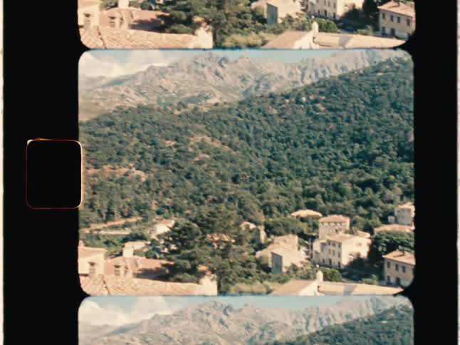 Super 8 film of a rural neighborhood in the mountain, the skyline with forest and mountains during a hot day