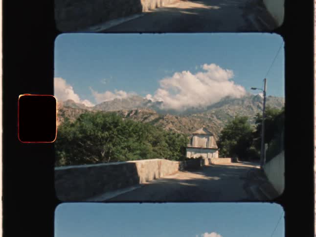 Super 8 film of a car driving through small roads which passes a church the mountains