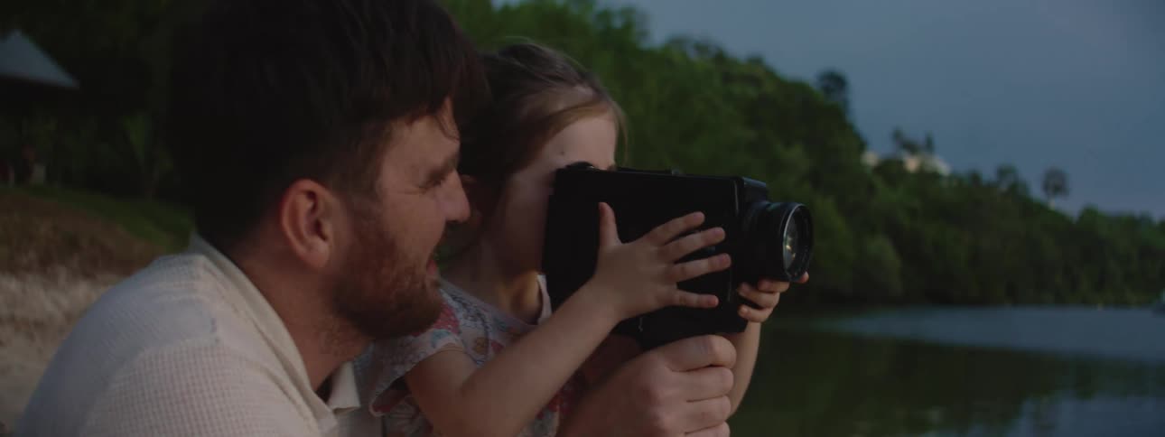 Father and his young daughter are enjoying a pleasant moment together they are holding a camera and viewing something captured by the camera