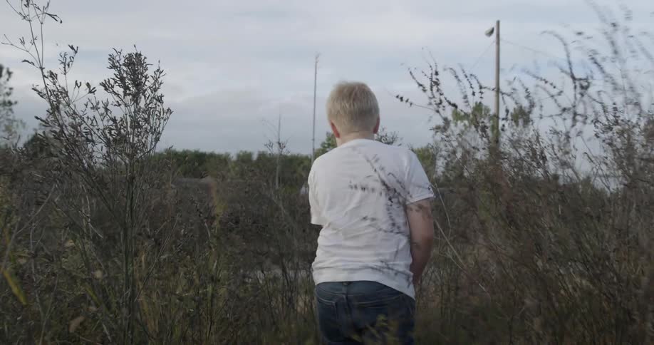 A boy is walking through some grass towards a trail