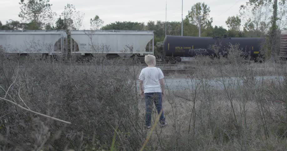 A boy walks through some grass to watch a train
