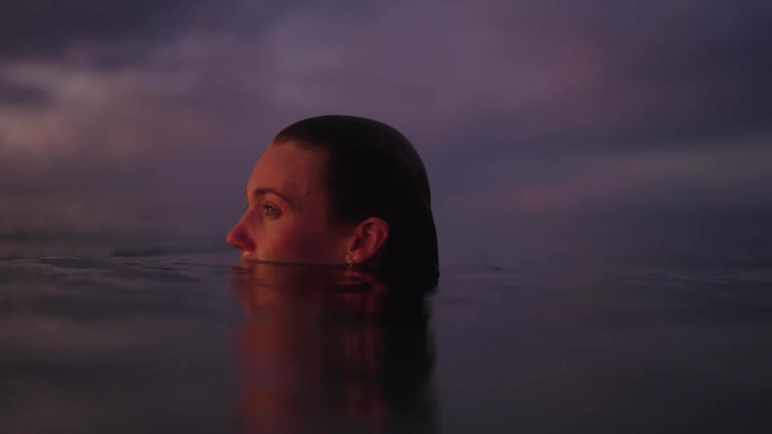 Portrait of a woman in the sea gazing at a sky with a reddish hue in the late afternoon