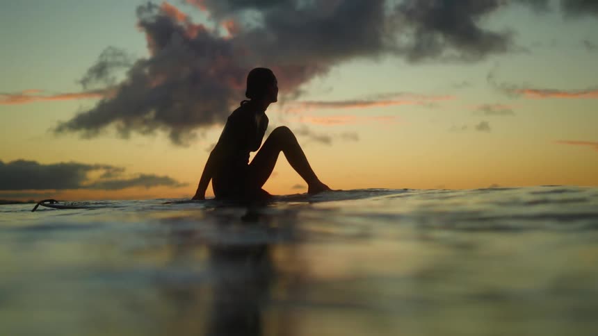 Silhouette of a woman in the water as the sun sets over the horizon