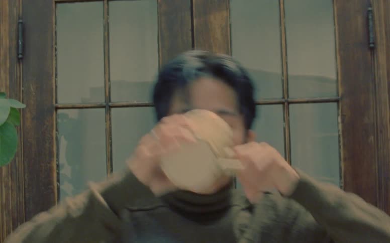 An asian man sipping from a cup and turning his face