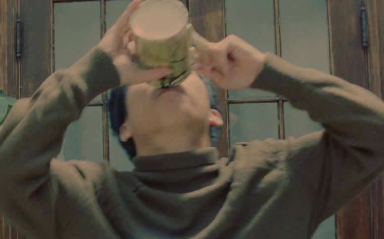 An asian man drinks something from a mug in dance performance movements