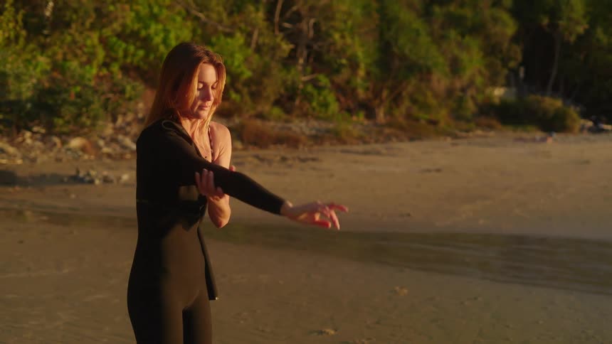 Beautiful young women putting on her wetsuit for a sunset surf