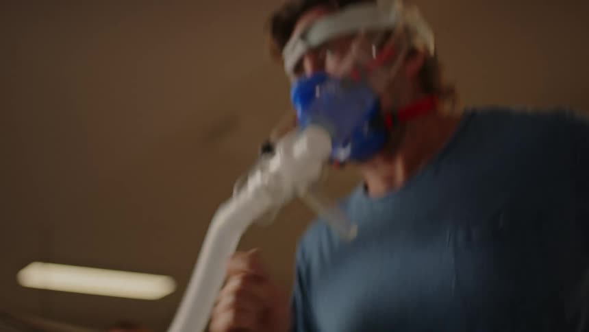 A man running on a treadmill with an oxygenation control mask accompanied by a doctor who is monitoring and speaking