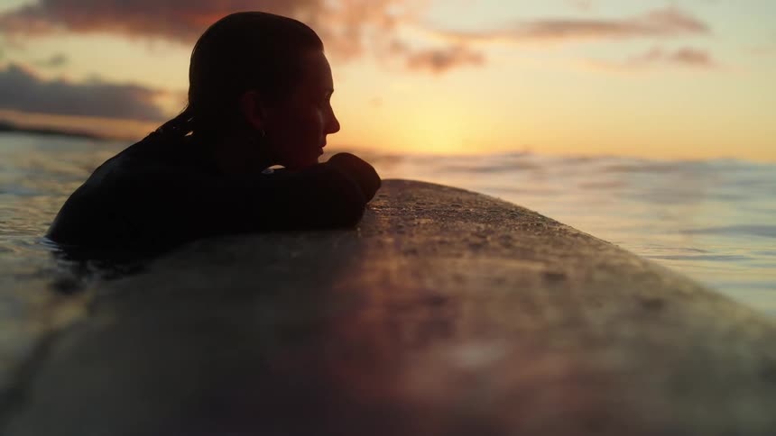 A woman with her hands resting on a surfboard gazing at the sea during a late afternoon