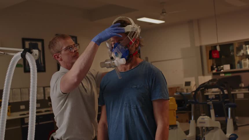 One man helps a second man put on a vo2 mask for a fitness test