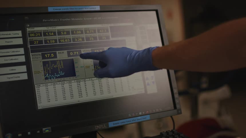 A person wearing surgical gloves is pointing at the monitor