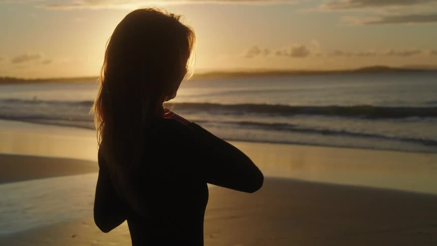 Beautiful young women adjusting wet suit at sunset